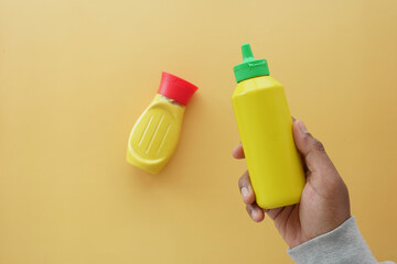 holding a bottle of mustard mayonnaise on yellow background 