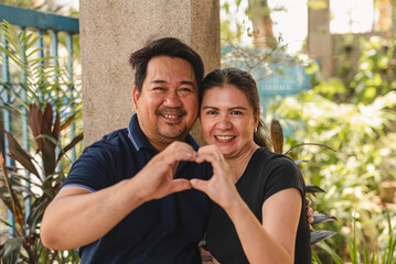 Middle aged Southeast Asian couple creates a heart with their hands, symbolizing love and two decades of togetherness.