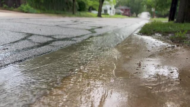 A fast moving current of Rain Water streams down the curb of a historic suburban neighborhood street after a rainstorm. A slice of life low angle video depicting light flooding after a storm.