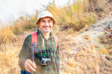 portrait asian senior man hiker in green checkered shirt wears hat, having a camera,holding trekking pole,concept elderly pensioner lifestyle,activity,travel,adventure