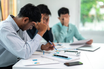 A man is sitting at a table with a pen and a piece of paper. He is looking at the paper and he is in deep thought. The other two men in the room are also looking at their papers
