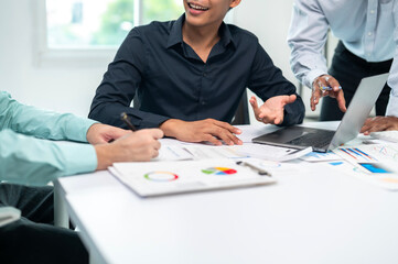 A group of people are sitting around a table with a laptop and papers. They are discussing something important
