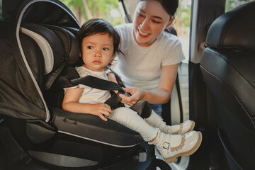 mother is fastening safety belt to toddler girl in car seat, safety baby chair travelling
