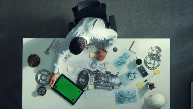 Top down view of skilled engineer writing and planning turbine engine design while sitting at meeting table with gear and electronic generator scatter around. Technician taking a note. Alimentation.