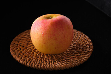 Close-up of apple placed on bamboo woven mat on solid color background
