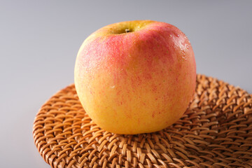 Close-up of apple placed on bamboo woven mat on solid color background