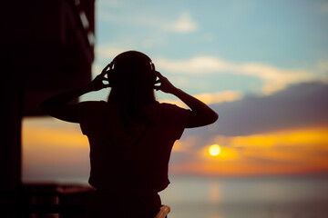 Silhouette of a Woman Listening to Music on a Sunset View. Happy girl wearing headphones admiring...