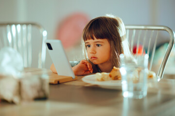 Little Girl Watching Cartoons on a Smartphone During Mealtime. Child having checking a phone during...