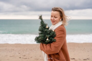 Blond woman Christmas tree sea. Christmas portrait of a happy woman walking along the beach and...