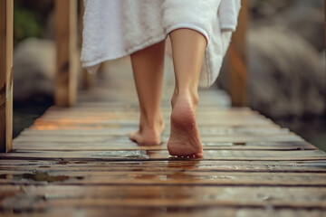Close up of a woman's feet walking on a wooden bridge in a spa center, focusing on the foot with a white towel around the waist, warm tones, natural light, high resolution 