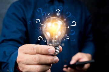Businessman holding glowing lightbulb and question mark with copy space for creative thinking idea.