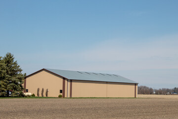 A large farm building next to a corn field.