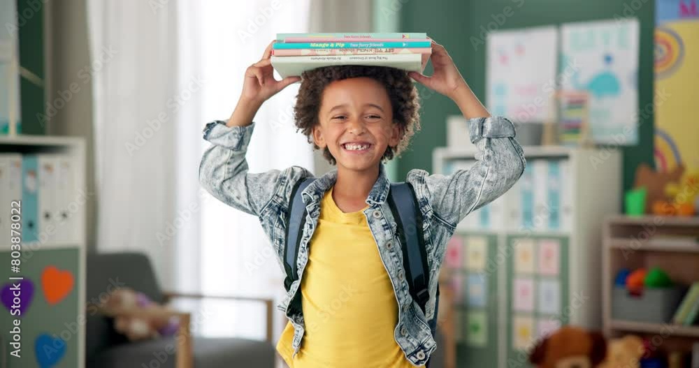 Poster Child, face and book on head in classroom for education learning in kindergarten, scholarship or happy. Kid, smile and knowledge academy for student creativity as reading lesson, excited or school