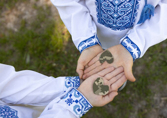 two children, dressed in traditional embroidered clothing, hold on palms heart cut out of...