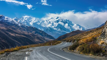Fototapeta premium Curving mountain road with hairpin turns and panoramic views of snow-capped peaks in the distance.