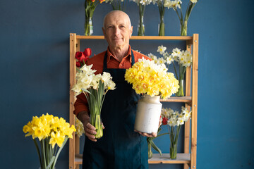 A pleasant-looking man seller holds two bouquets of beautiful daffodils in his hands.