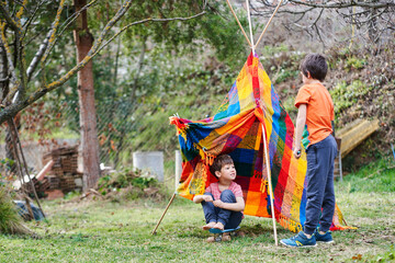 Siblings playing with a tepee in the backyard.