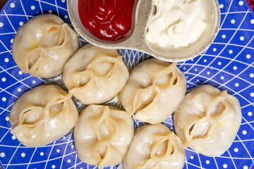.manti and sauce on a blue plate on a burgundy background