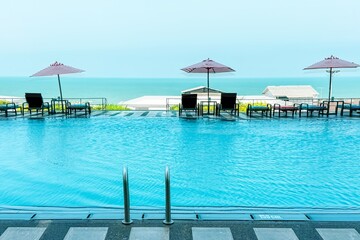 Inviting resort pool overlooks the ocean, with stylish purple umbrellas and cozy lounge chairs set...