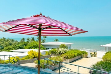 Striped pink and white umbrella stands prominently on terrace overlooking serene beachfront,...