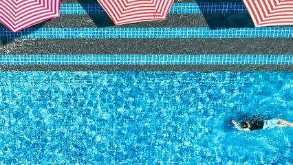 lone swimmer enjoys the tranquil waters of a resort pool, framed by stylish striped umbrellas,...