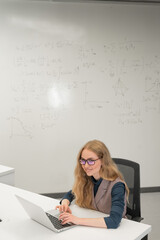 Caucasian woman scientist typing on laptop. White board with formulas. Vertical photo. 