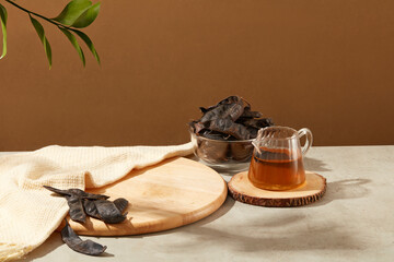 A cutting board displayed with beige scarf, a bowl of black locust fruits and a cup of black locust liquid. Vacant space on the cutting board to show products that extracted from Black Locust