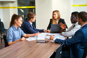 Female CEO leads business meeting in modern boardroom. Multiethnic execs engage in team discussion...