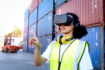 African woman worker with safety vest helmet wears virtual reality glasses at shipping cargo container yard. Female engineer works with digital technology for industrial revolution logistic control.