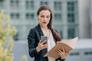 business woman with document folder on the street looking at mobile phone