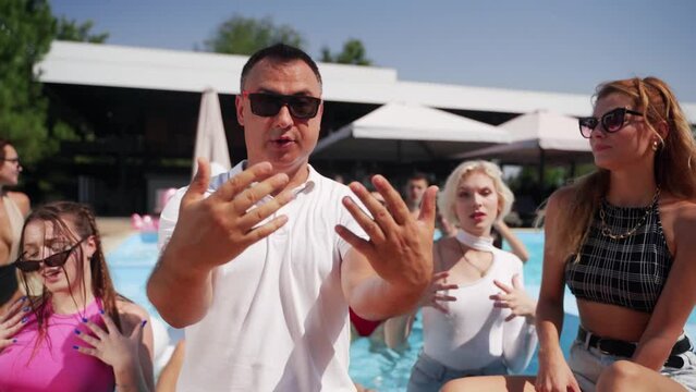 Models dance, twerk, sing and relax with alcohol cocktails at swimming pool party on weekends. Male and female flirt, send kisses, pose in bright swimsuit and sunglasses and show slim tanned body.
