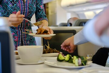 A flight attendant serves a plate of traditional Malaysian chicken sate skewers with peanut sauce, rice cakes, sliced cucumber red onion as an appetiser on a business class flight from Sydney to KL