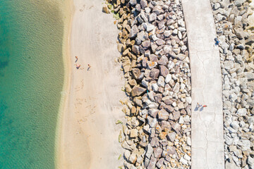 drone aerial top view of the shore of a beach with people next to a breakwater