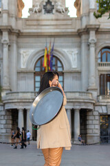 A young woman, seen from behind, carries a paella pan while walking through the city downtown