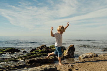 little blond boy playing on the seashore. child playing on the seashore. boy stands on stones in the water. child playing on the seashore