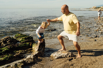 father supports son on rocks in the sea. Shot of father helping his son to jump over the rock on...