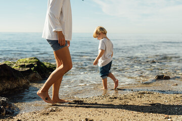little blond boy playing on the seashore. child playing on the seashore. boy stands on stones in the water. child playing on the seashore