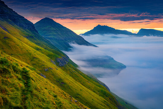 Dramatic morning view of Faroe Islands with huge fog on fjord, Denmark, Europe. Fantastic summer scene of Eysturoy island, Funningur village location. Beauty of nature concept background.