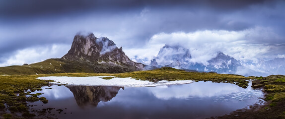 Panoramic view of rock formation with reflection tarn and the Nuvolau group of mountais in the background in Italian Dolomites on cloudy day. Giau Pass.