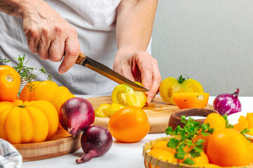 A woman is preparing a tomato salad. Ripe vegetables, herbs, aromatic spices, olive oil
