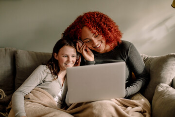 Smiling young woman and teenage girl watching movie together on laptop at home