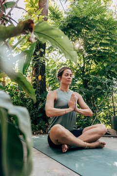 Mature woman practicing meditation while sitting cross-legged amidst plants at wellness resort