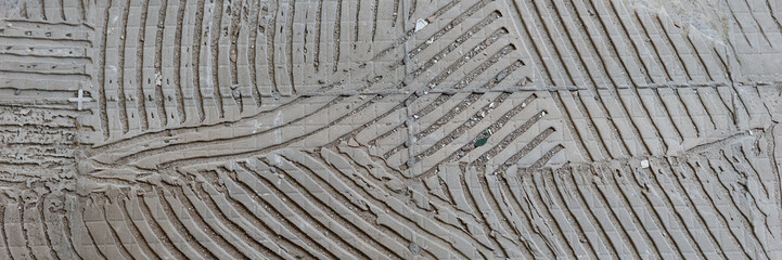 Panoramic image. Background of old grey tile adhesive on the floor. Abstract pattern of notched trowel