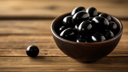  A bowl of shiny black olives on a wooden surface
