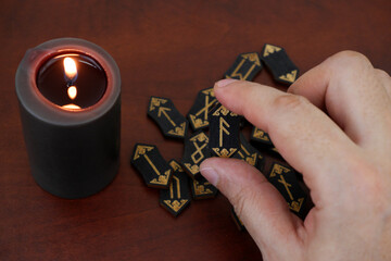 Burning candle and wooden runes on table. Human hand shows rune ansuz.