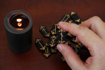 Burning candle and wooden runes on table. Human hand shows rune nauthiz.	