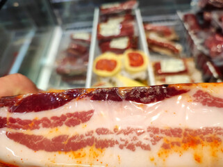Seasoned  bacon in packaging in a supermarket against the background of a refrigerator with salami