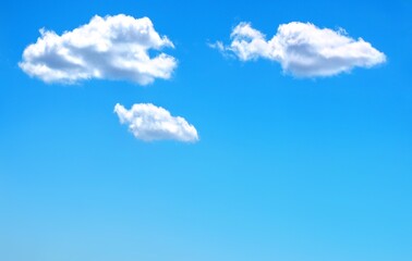 Three isolated white clouds in a clear blue sky with space for text.