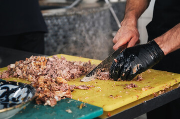 male chef cut boiled beef meat with knife on a cutting board for cooking Uzbek pilaf in kitchen at...