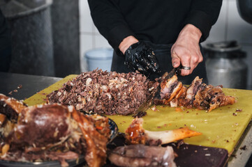 man chef cut boiled beef meat with knife on a cutting board in kitchen at a restaurant in Tashkent...